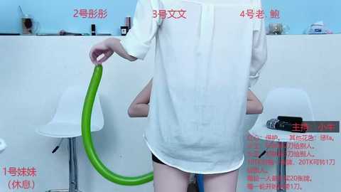 Media: Video of a person in a white dress, holding a green hose, in a sterile, clinical room with white walls and a blue ceiling, labeled with Chinese text and numbers.