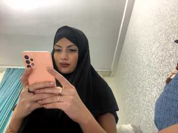 Media: Video of a young South Asian woman with light brown skin, wearing a black hijab and black t-shirt, taking a selfie in a bathroom with a pink iPhone.