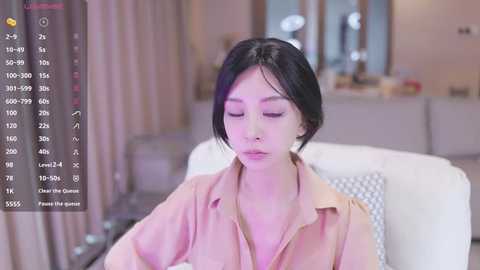 Media: A video of an East Asian woman with short black hair, wearing a beige blouse, sitting on a white couch in a modern living room.