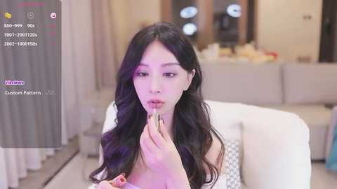 Media: Video of an Asian woman with long black hair, wearing a white dress, holding a straw in a prayer-like pose in a modern living room.