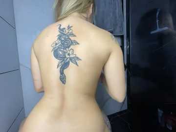 Media: Video of a topless blonde woman with a large, intricate black dragon tattoo on her back, standing in a dimly lit bathroom with a shower curtain and white tiles.