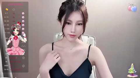 Media: A video of a young Asian woman with fair skin and dark hair in a messy bun, wearing a black spaghetti-strap dress. She sits in a white chair, with a virtual character overlaid in the corner.