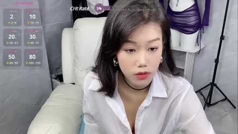 Media: Video of an East Asian woman with straight black hair, wearing a white blouse, sitting on a white leather couch in a modern, minimalist room.