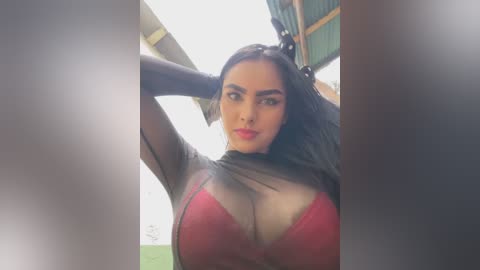 Media: Video of a South Asian woman with long black hair, wearing a sheer black top and a red lace bra, posing confidently outdoors.