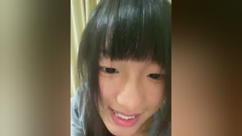 Media: Video of an Asian girl with straight black hair and bangs, smiling, wearing a light blue shirt, against a beige background.