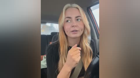 Media: A video of a blonde woman in a black jacket, seated in a car with a beige seatbelt, wearing a confused expression, while looking out the window.