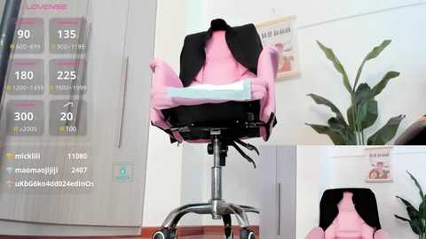 Media: Video of a pink baby carrier with black straps hanging on a metal stand in a modern, minimalist room with white walls and a potted plant.