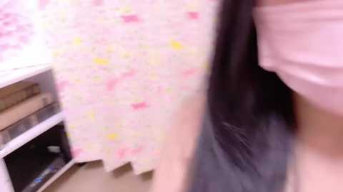 Media: A video of a young woman with long, dark hair, wearing a light pink t-shirt, standing in a kitchen with pink floral wallpaper and a white oven.