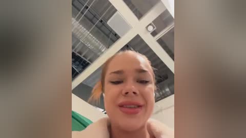 Media: A video of a young woman with light skin and blonde hair, smiling, standing in a modern, industrial kitchen with white cabinets and exposed pipes.