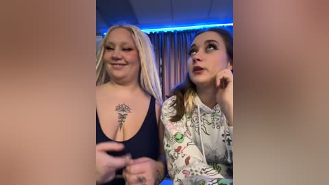 Media: Video of two women, one blonde with a tattoo, wearing a black top, and another with brown hair, wearing a floral dress, looking thoughtful in a dimly lit room with blue lighting.