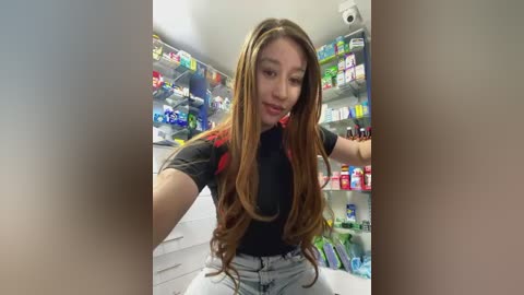 Media: Video of a young Asian woman with long, straight brown hair, wearing a black t-shirt and light blue jeans, shopping in a brightly lit convenience store with colorful shelves of snacks and beverages in the background.