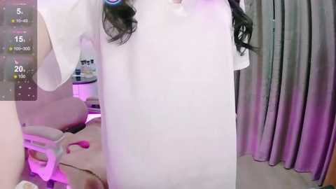 Media: A video of a woman in a white dress, standing in a bedroom with purple lighting, curtains, and a bed in the background.