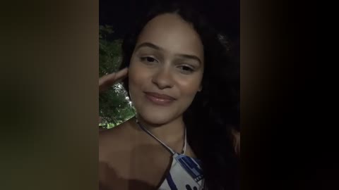 Media: Video of a young woman with light brown skin and long black hair, smiling, wearing a blue and white striped top, set against a dark, blurred background.