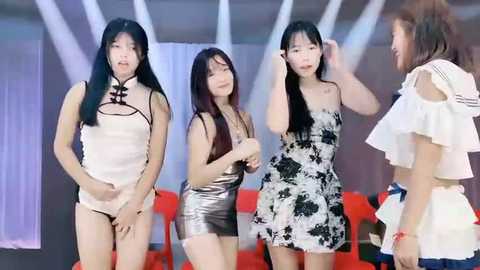 Media: Video of four Asian women in casual dresses, one with long black hair, standing indoors with red couches and white curtains in background.