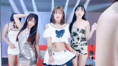 Media: Video of four East Asian women in provocative schoolgirl outfits, with one wearing a blue bow, in a modern, minimalist room with white walls and red accents.