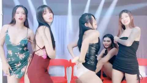 Media: Video of four Asian women, each with long black hair, wearing revealing black or red dresses, smiling, posing in a modern, brightly lit room with white and red decor.