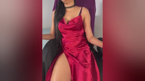 Media: Video of a woman in a deep red satin dress with a thigh-high slit, sitting on a black chair, wearing a black choker necklace, against a purple backdrop.