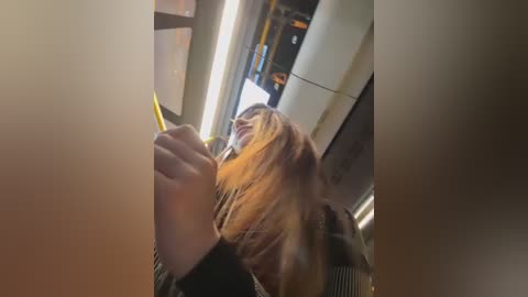 Media: Video of a woman with long, blonde hair, wearing a black jacket, using a yellow pen while seated in a dimly lit, modern train compartment.