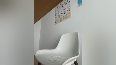 Media: Video of a minimalist, modern room with a white plastic Eames chair against a plain white wall. Above the chair, a calendar with Japanese characters hangs. The room is well-lit with natural light.