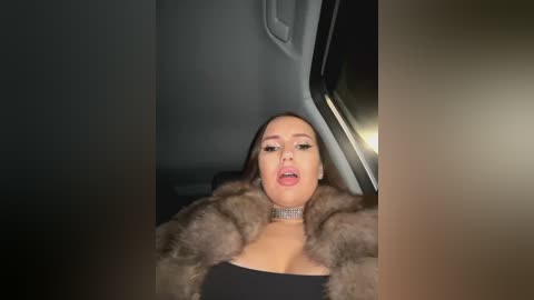 Media: A video shows a woman with long brown hair, wearing a fur coat and a black top, sitting in a car at night, mouth slightly open, eyes half-closed, and dim lighting.