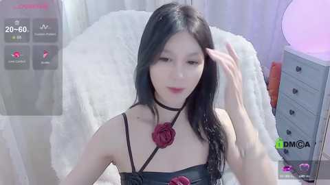 Media: A video of an East Asian woman with long black hair, wearing a black leather corset with a red rose, and a choker, sitting on a white fur blanket.