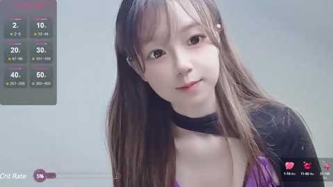 Media: Video of a young Asian woman with long brown hair and fair skin, wearing a black top, captured in a live stream. Background is a light-colored room.