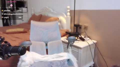 Media: A video of a white office chair with a blue cushion on a bed, surrounded by a cluttered bedroom with a white nightstand and a TV.