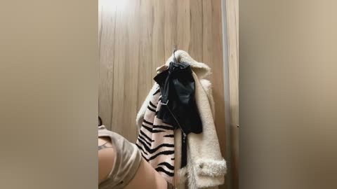 Media: Video of a beige zebra-patterned robe hanging on a wooden door with a black leather bag and fluffy white coat draped over it.