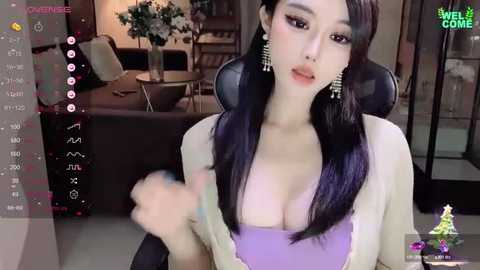 Media: A video of a young East Asian woman with long, straight black hair, wearing a purple top, sitting on a black chair in a modern, dimly lit living room.