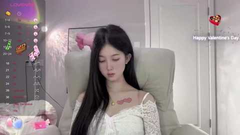 Media: A video of an Asian woman with long black hair, wearing a white lace dress, sitting in a beige armchair, surrounded by a virtual chat room with heart icons and a \"Happy Valentine's Day\" message.