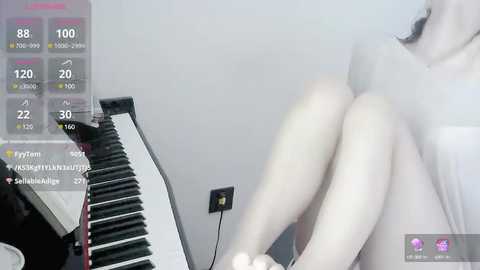 Media: Video of a pale-skinned, slender, nude woman with dark hair, sitting on a bed with a black desk lamp and a power strip. Background shows streaming stats and a white wall.