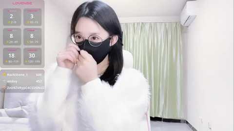 Media: A video of an East Asian woman with straight black hair and glasses wearing a black face mask in a hospital room with white curtains and a bed.