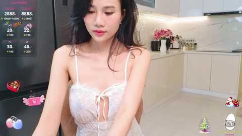 Media: Video of an Asian woman with long black hair, fair skin, and a slender physique, wearing a revealing white lace lingerie top, in a modern kitchen.