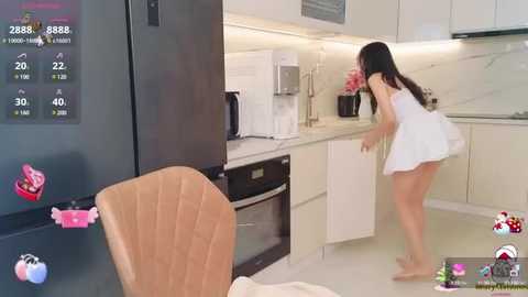 Media: Video of a woman in a white dress bending over in a modern kitchen, with a large fridge displaying food labels and a clock, and a wooden chair nearby.