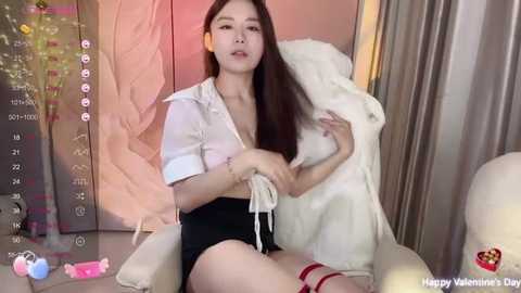 Media: Video of a young Asian woman with long black hair, wearing a white top and black shorts, holding a white teddy bear, surrounded by pink and white Valentine's Day-themed decorations.