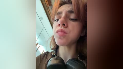 Media: Video of a young Caucasian woman with light brown hair, wearing headphones, making a pouty face. She stands in a brightly lit room with modern, clean decor.