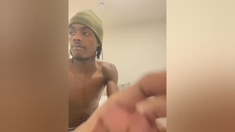 Media: A blurry video of a shirtless, dark-skinned man with dreadlocks, wearing a green beanie, looking upwards, in a dimly lit room.