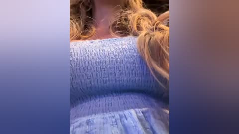 Media: A close-up video of a woman's chest, showing light blue ribbed fabric, possibly a bra, with her long, wavy blonde hair partially covering the image.