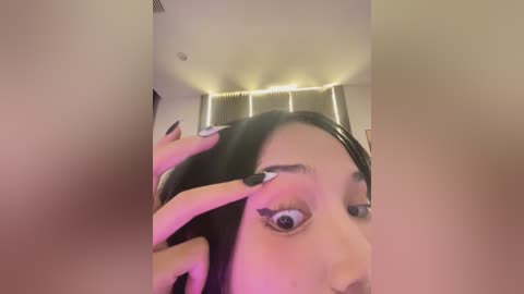 Media: A video of a woman with long black hair and dark eyeliner, looking surprised, taken from a low angle, showing her face and hands.