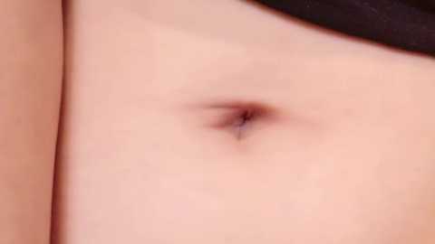 Media: Close-up video of a light-skinned person's navel, showing a small, darkened area surrounded by smooth skin. The background includes a hint of black fabric.