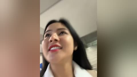 Media: Video of a smiling woman with long black hair, wearing a white blouse, in a blurred office setting.