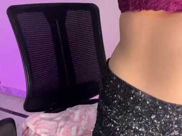 Media: A close-up video of a person's midsection, showing their bare back and waist, partially clad in black glittery leggings. In the background, a black office chair and a pink and white patterned shirt are visible. The lighting is soft, with a purple hue.