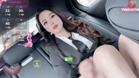 Media: Video of an Asian woman with long, wavy hair, wearing a black suit, reclined in a car seat, with a smartphone showing a \"Lounge\" app screen in the background.