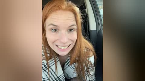 Media: Video of a smiling woman with long red hair and pale skin, wearing a checkered coat, leaning into a car window.