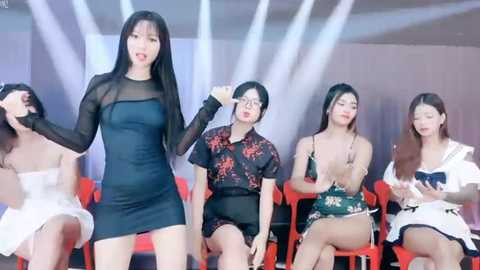 Media: Video of five East Asian women in contemporary fashion, performing on a stage with red chairs, white curtains, and bright lighting.