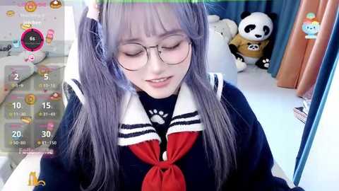 Media: Video of an East Asian woman with long, lavender hair and glasses, wearing a navy blue sailor-style school uniform with a red tie and white collar, sitting in a cozy room with a stuffed panda and a pink teddy bear.