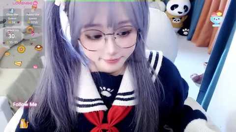 Media: Video of a young girl with long, lavender hair in pigtails, wearing glasses and a navy blue sailor dress with a red bow, sitting indoors near a window, with a playful virtual reality game interface overlay.