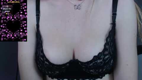 Media: Video of a fair-skinned woman in black lace bra, with a silver necklace, partially cropped face. Background includes a screen with heart emojis and a \"LOVE\" overlay.