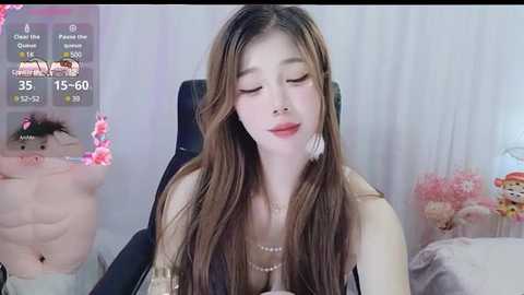 Media: A video of an Asian woman with long brown hair, wearing a pearl necklace, sitting in a black office chair, eyes closed, in a room with pink and white decor.