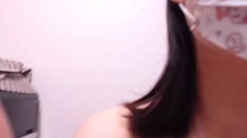 Media: Video of a woman with straight, dark brown hair, partially visible from the back. She is in a bathroom with a white wall and a shower curtain with floral patterns.